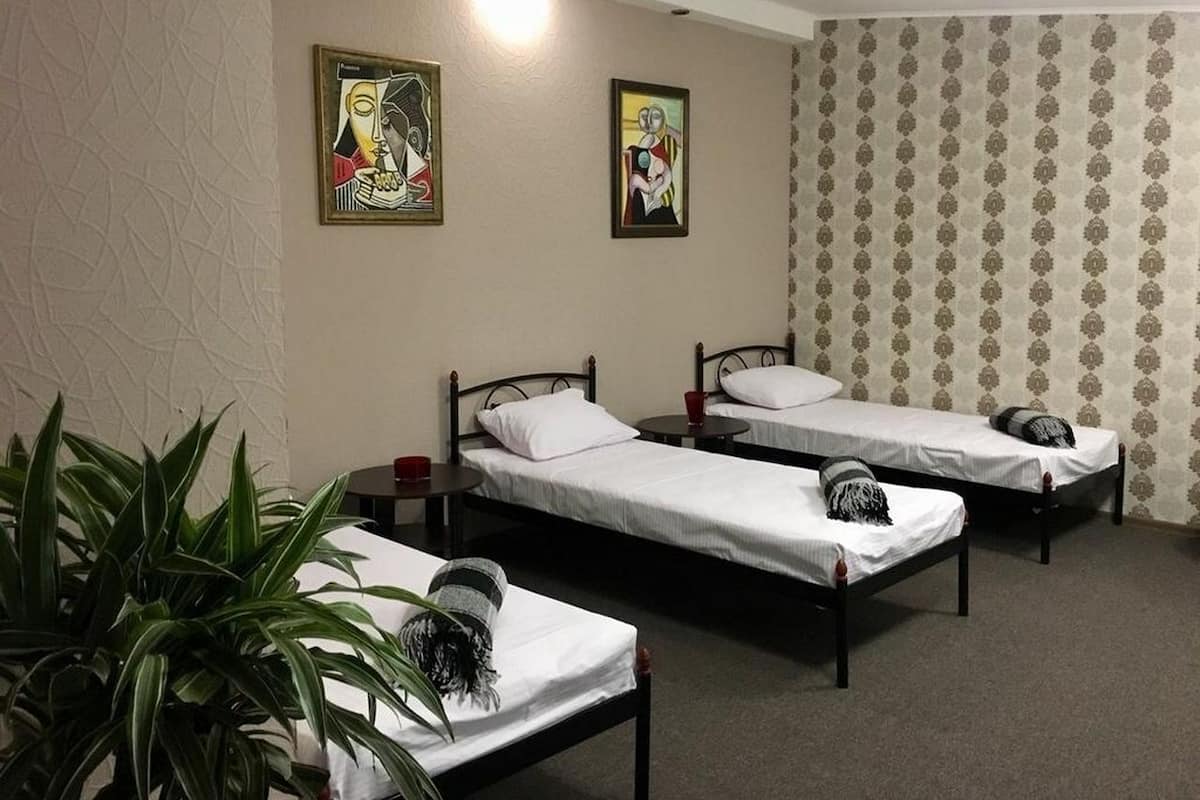 A room with three single beds, a small table, a red cup, and two framed artworks on the wall.