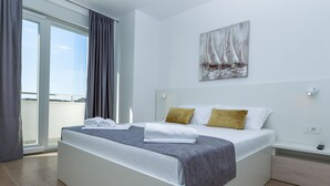 Quarto de hotel moderno com uma cama grande, vista através de uma porta deslizante e um quadro na parede.