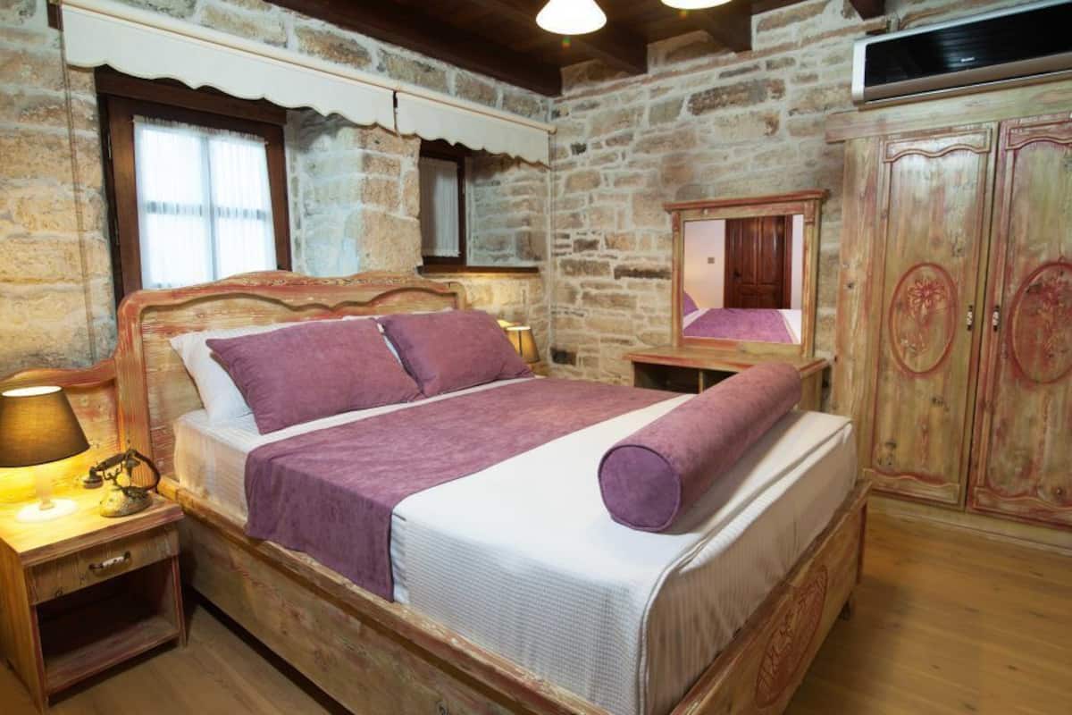 Quarto rústico com cama de madeira, mesa de cabeceira com luminária, guarda-roupa de madeira e parede de pedra.
