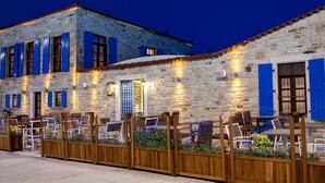 A stone building with blue shutters and outdoor seating. - 1922 Hotel (Foça)