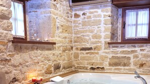 A stone-walled bathroom with a wooden bathtub, a wooden bench, and a towel rack. - 1922 Hotel (Foça)