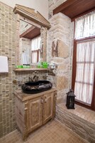 Un baño con pared de piedra, tocador de madera y un espejo grande.