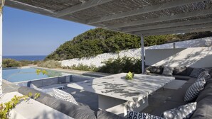 An outdoor seating area with a pool, stone walls, and a view of the sea.