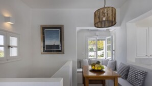 A modern interior with a wooden table, a bench with patterned cushions, a framed picture, and a hanging light fixture.