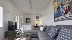 A modern living room with a grey sofa, a glass coffee table, a TV, and a framed picture on the wall.