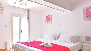 Ein Schlafzimmer mit Bett, weißen Wänden, einer roten Decke, einem Nachttisch, einer Lampe und einer Tür.