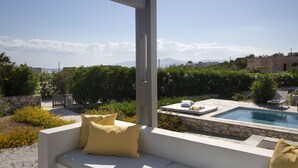 Un espace aménagé au bord de la piscine, avec un canapé blanc et des coussins, une piscine en pierre et une vue sur un paysage montagneux.
