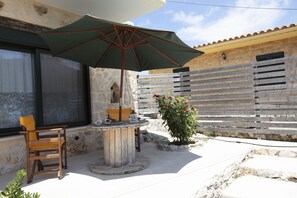 An outdoor patio with a wooden table and chairs, a green umbrella, and a potted plant.