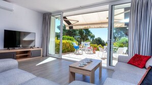 Un salon moderne doté d’un téléviseur à écran plat, de canapés gris, d’une table basse en bois et d’une porte-fenêtre coulissante donnant sur un patio extérieur avec des chaises et une table.