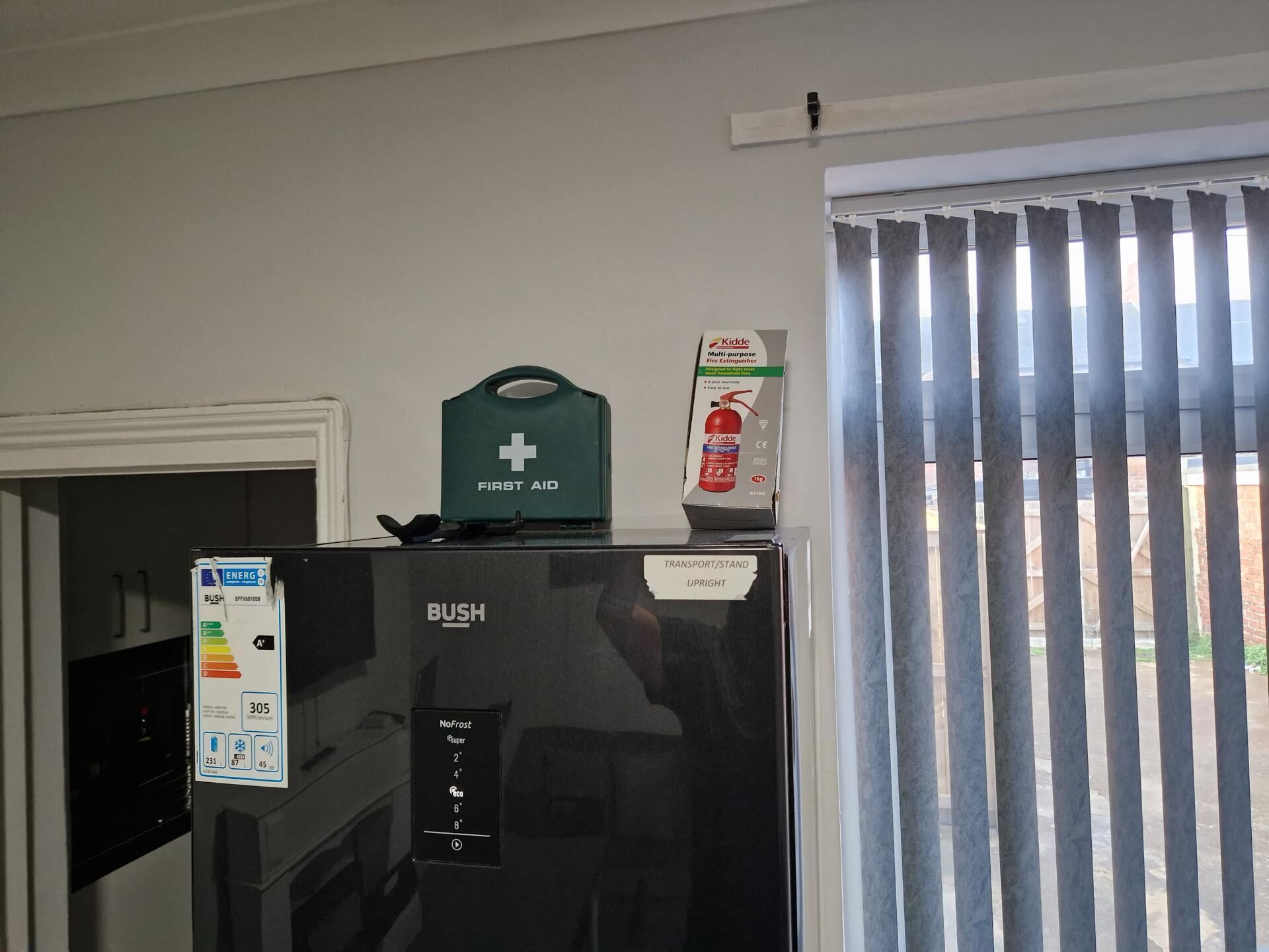 A black refrigerator with a 'BUSH' brand label, a 'NoFrost' control panel, a 'First Aid' kit, and a 'Kidde' fire extinguisher on top.