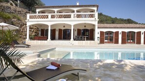 Un bâtiment à deux étages avec une piscine, des chaises longues et un livre posé sur une table.