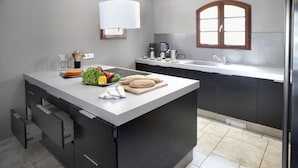 Une cuisine moderne dotée d’un îlot central, de meubles de rangement aux couleurs sombres, d’une fenêtre et d’un évier encastré.