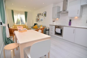 A modern kitchen with white cabinets, a built-in oven, and a dining area with a table and chairs.
