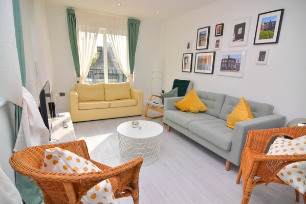 A living room with two sofas, wicker chairs, a round coffee table, and a TV.