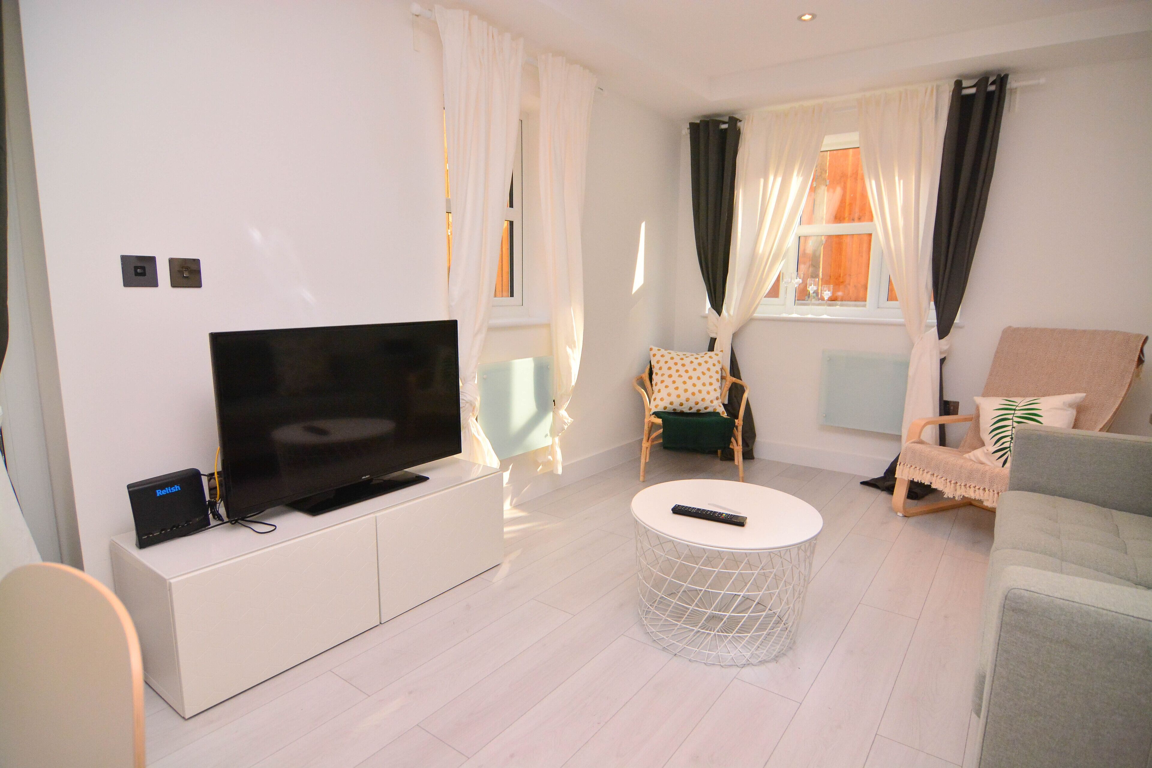 A modern living room with a flat-screen TV on a white cabinet, a round coffee table, and two chairs with cushions.