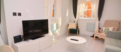 A modern living room with a flat-screen TV on a white cabinet, a round coffee table, and two chairs with cushions.