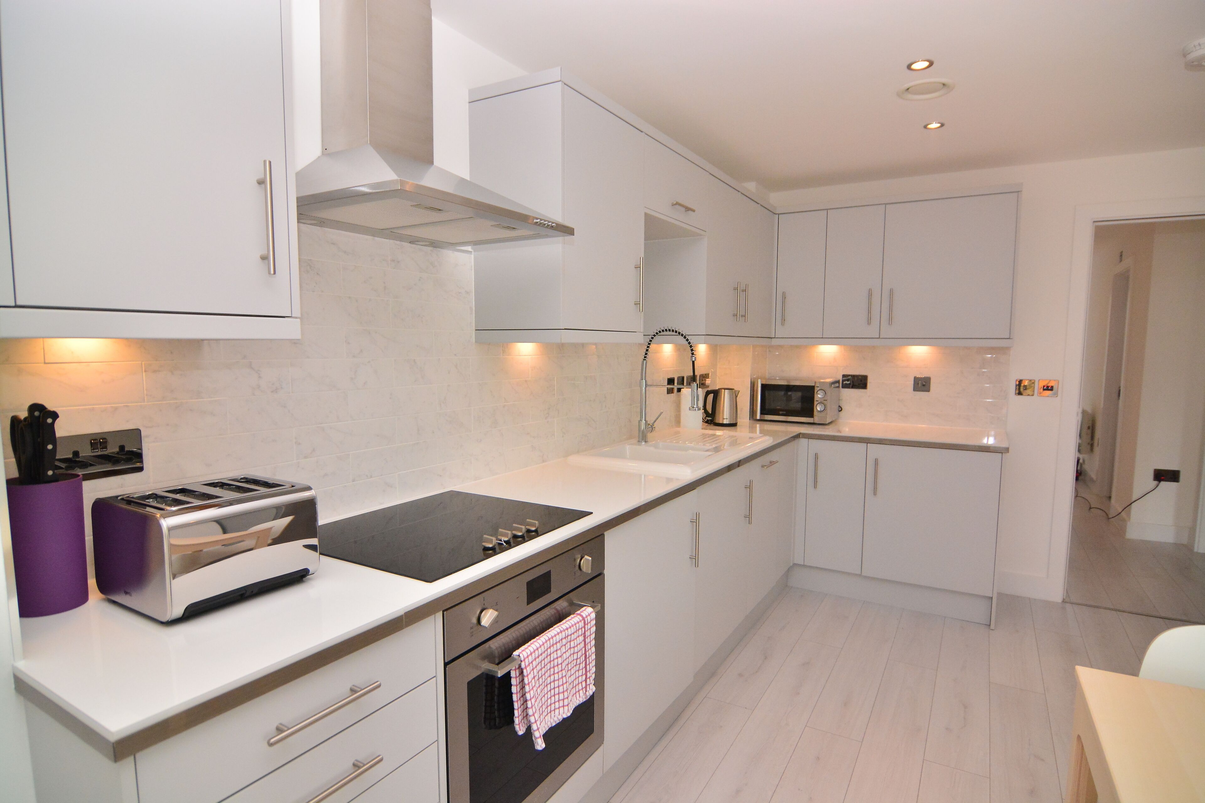 A modern kitchen with white cabinets, a built-in oven, a microwave, and a toaster.