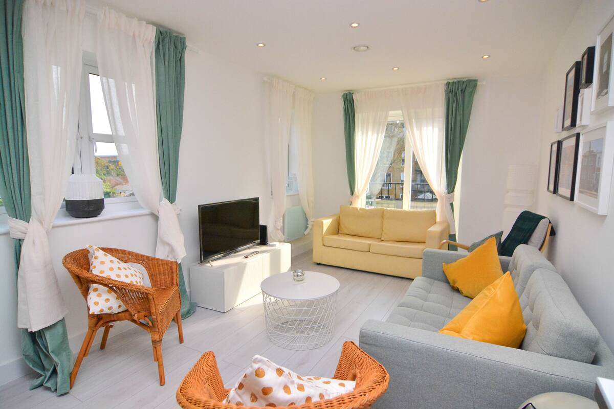 A modern living room with a grey sofa, orange wicker chairs, a white coffee table, and a flat-screen TV.