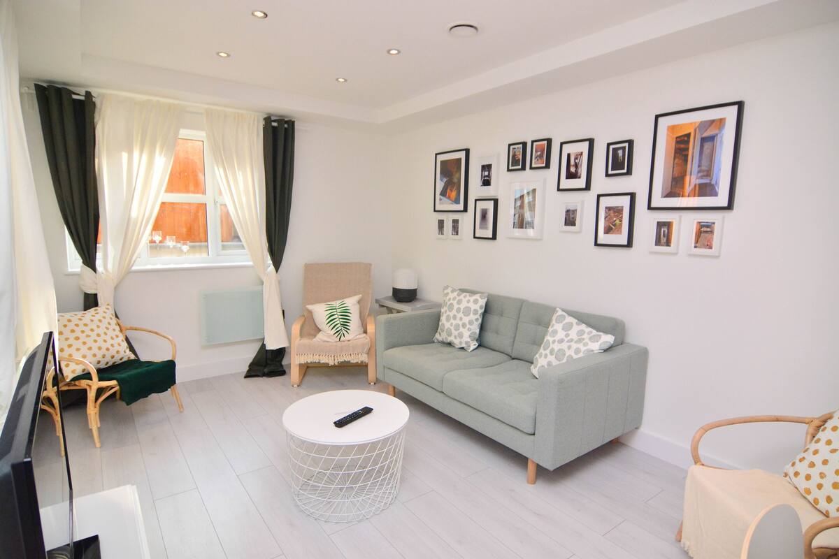A modern living room with a grey sofa, two armchairs, a round coffee table, and a flat-screen TV.