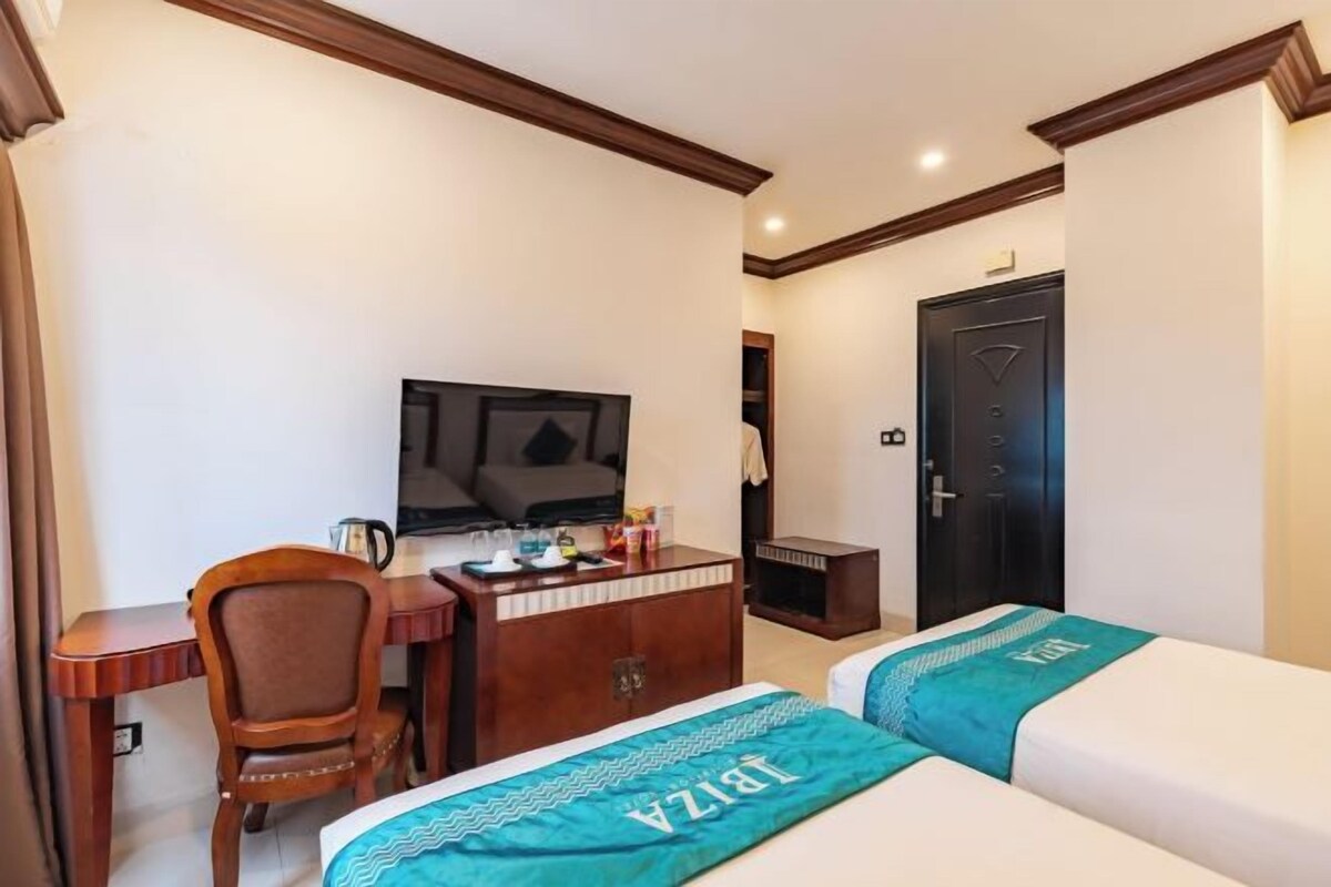 A hotel room with a bed, a desk, a chair, a television, and a door.