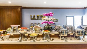 A buffet setup with various food items and a floral centerpiece. - IBIZA Riverfront Da Nang Hotel (Da Nang)