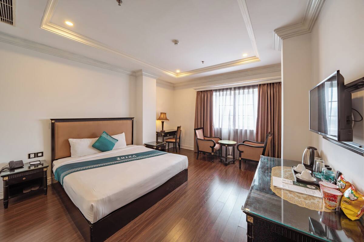 A hotel room with a large bed, a desk with a chair, a television, and a window with curtains.