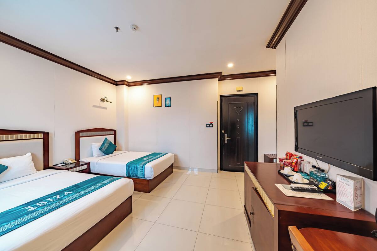 A hotel room with two beds, a desk with a TV, and a minibar.