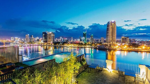 A nighttime cityscape with a large, illuminated swimming pool and a view of the city skyline. - IBIZA Riverfront Da Nang Hotel (Da Nang)