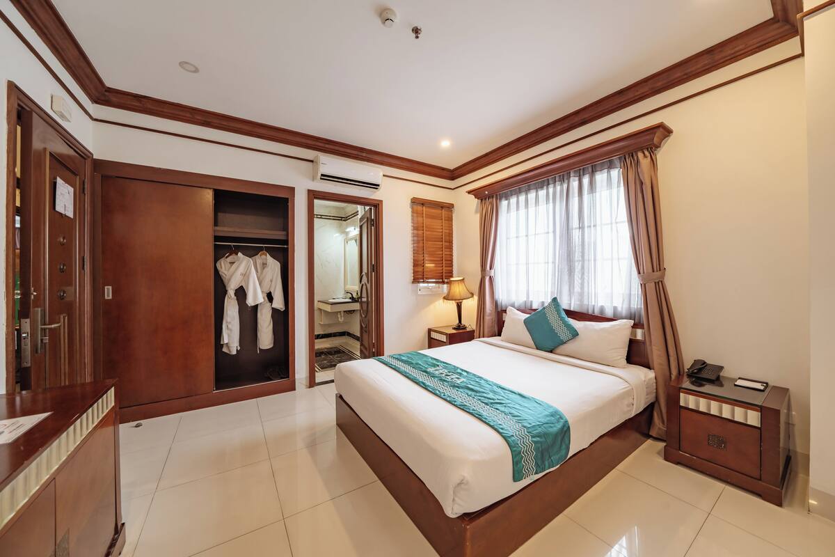 A hotel room with a large bed, a wardrobe, a mirror, and a bedside table with a lamp.