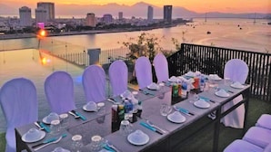 A table set for a meal with a cityscape and mountains in the background. - IBIZA Riverfront Da Nang Hotel (Da Nang)