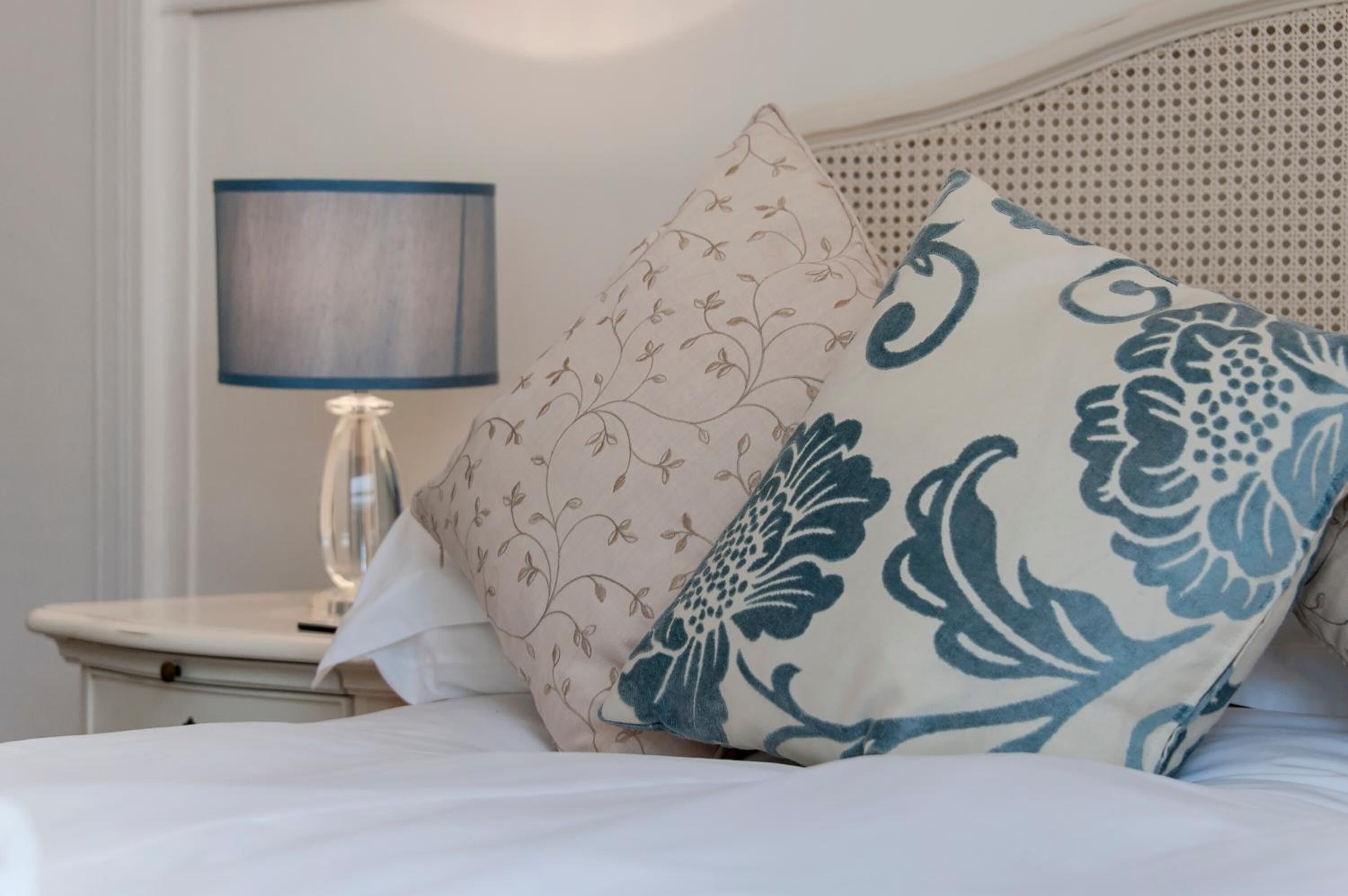A neatly made bed with floral-patterned pillows and a bedside table with a lamp.