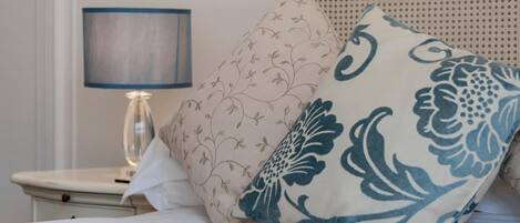 A neatly made bed with floral-patterned pillows and a bedside table with a lamp.