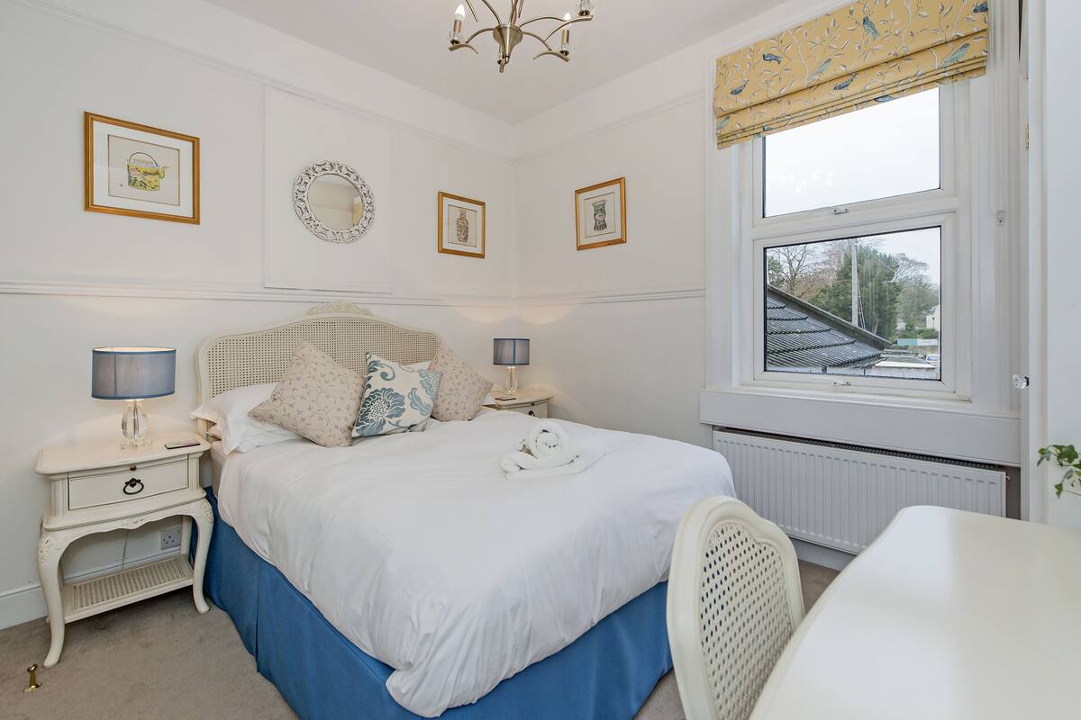 A neatly arranged bedroom with a bed, bedside tables, a lamp, and a window with a view.