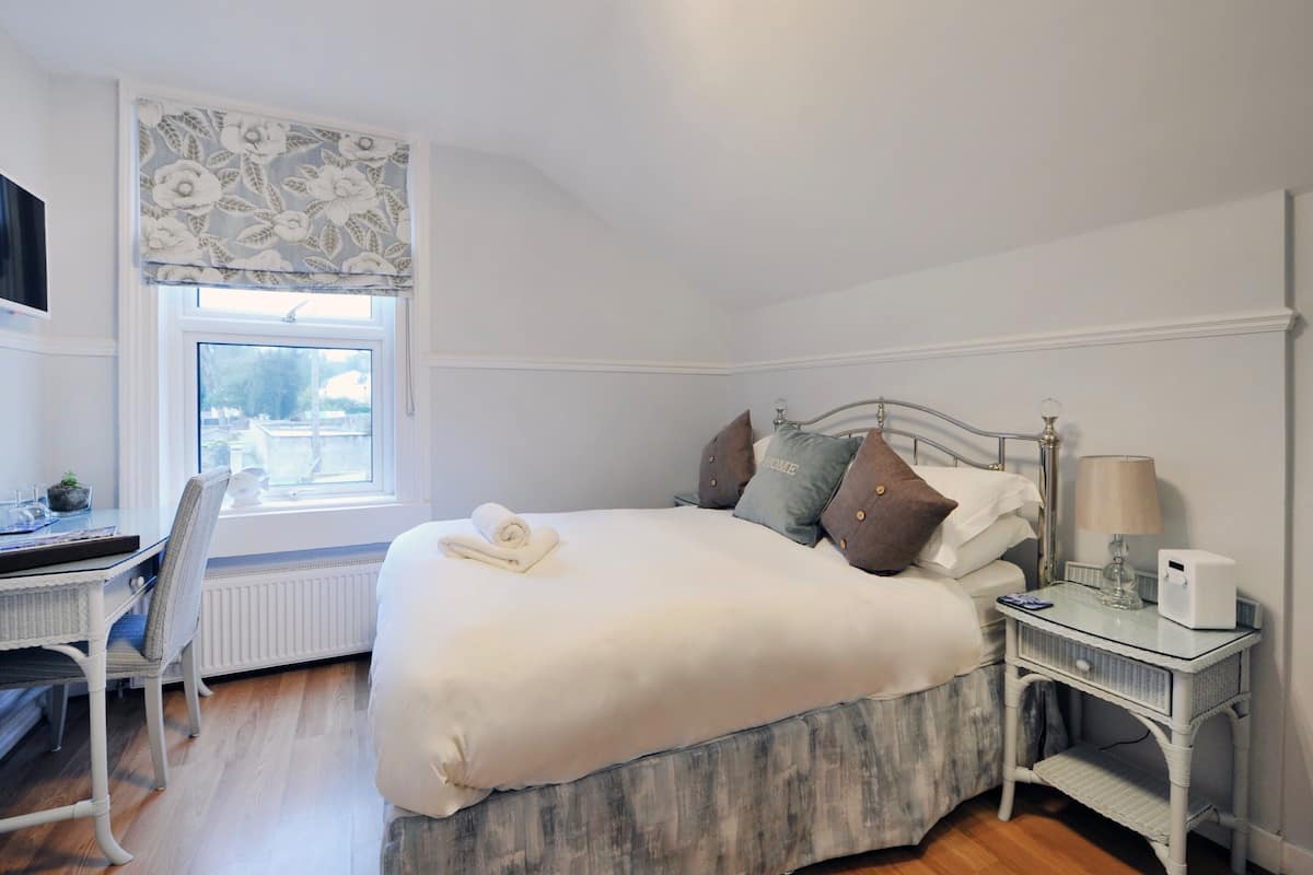 A bedroom with a bed, a bedside table with a lamp, a chair, a window with a view, and a radiator.