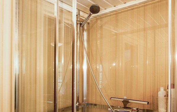 A shower with a handheld showerhead, a glass door, and a wooden panel wall.
