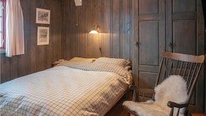 Une chambre à coucher avec un lit, une chaise, des murs en bois et une lampe fixée au mur.