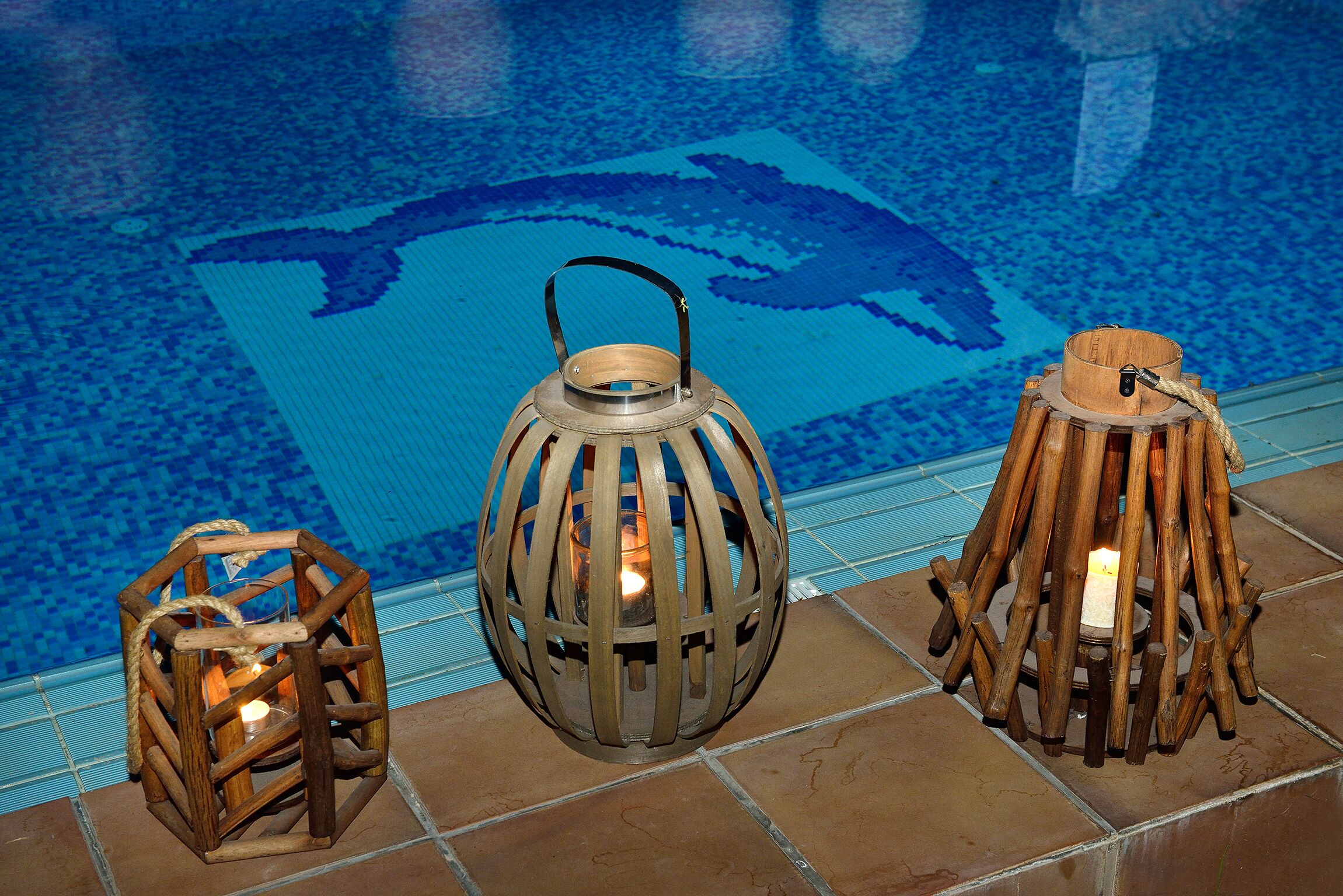 Three wooden lanterns with candles by a poolside.