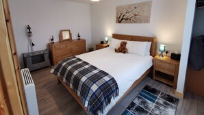 Une chambre à coucher avec un lit, une commode en bois, des tables de chevet, une lampe, un ours en peluche et un tableau accroché au mur.