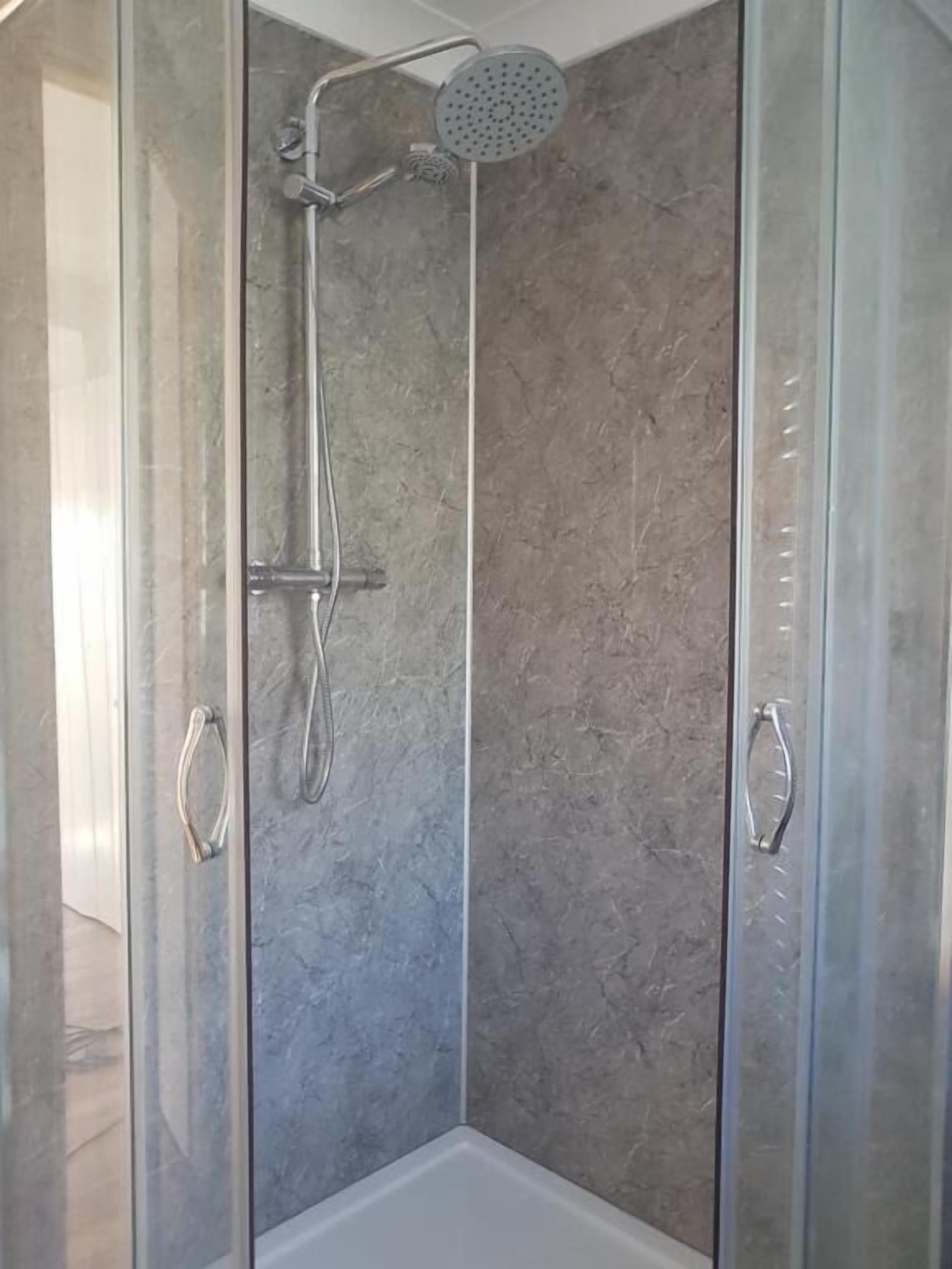 A glass-enclosed shower stall with a handheld showerhead and a wall-mounted faucet.