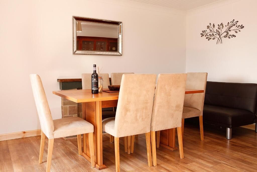 Un comedor con una mesa de madera y cuatro sillas, un sofá negro, un espejo y un adorno en la pared.