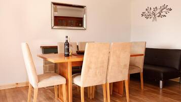 A dining area with a wooden table and four chairs, a black sofa, a mirror, and a wall decoration.
