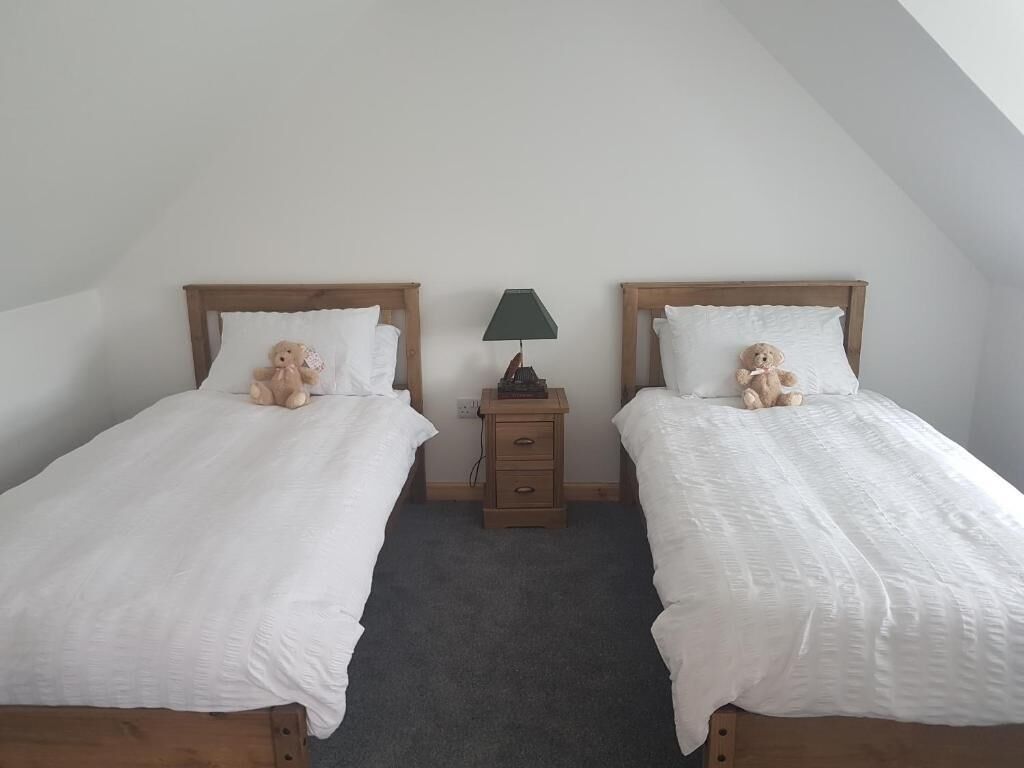 A bedroom with two single beds, each with a wooden headboard, white bedding, and a small bedside table with a lamp.