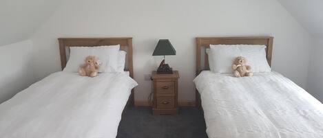 A bedroom with two single beds, each with a wooden headboard, white bedding, and a small bedside table with a lamp.
