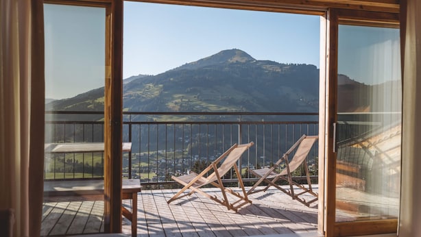 A balcony with wooden flooring and two wooden chairs, overlooking a mountainous landscape.