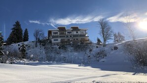 A multi-story building with balconies, surrounded by snow-covered trees and a clear sky.