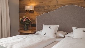 A hotel room with two beds, a nightstand with a vase of flowers, and a wall-mounted lamp.