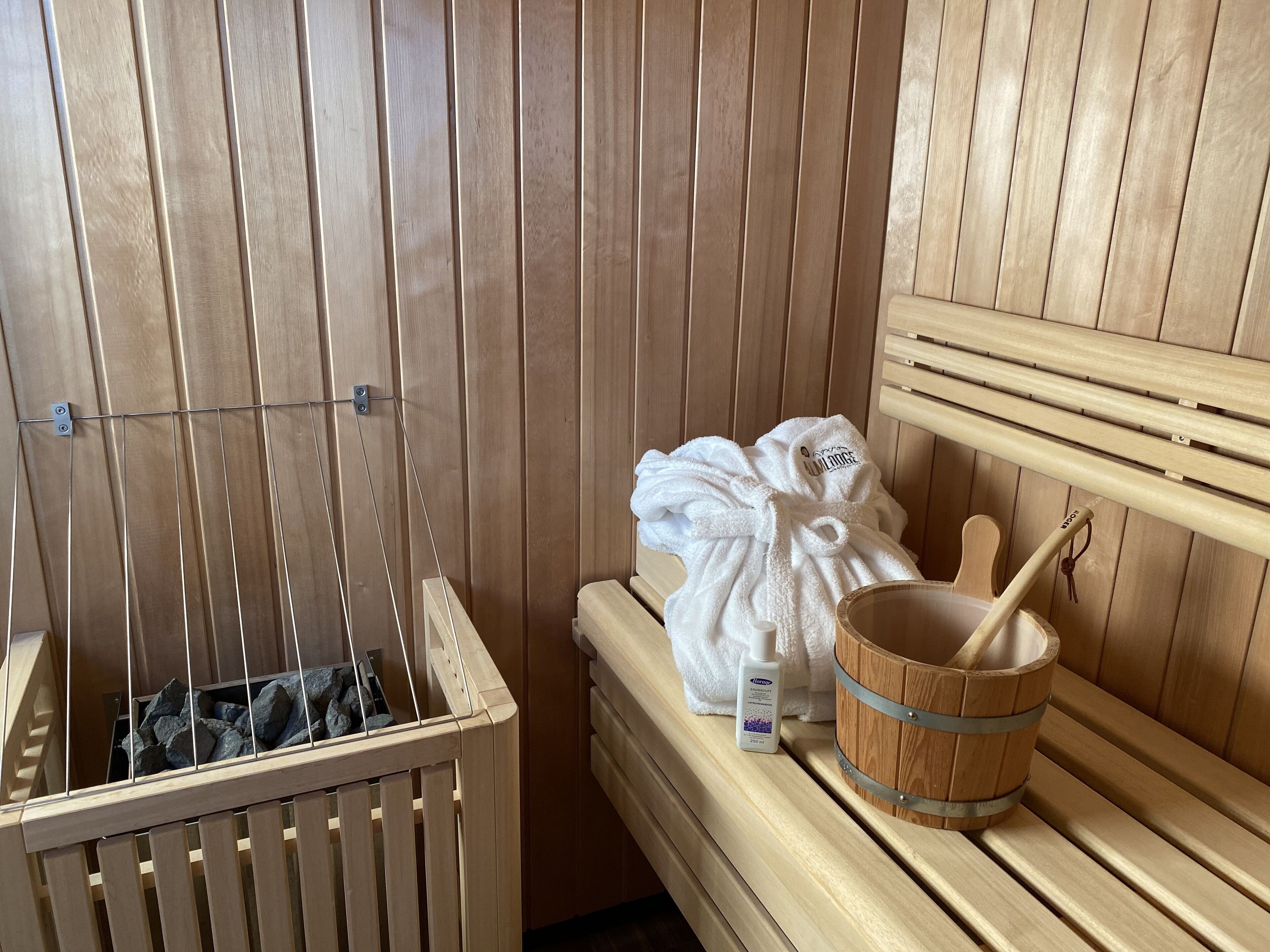 Un sauna avec des bancs en bois, un seau en bois et une bouteille de lotion.