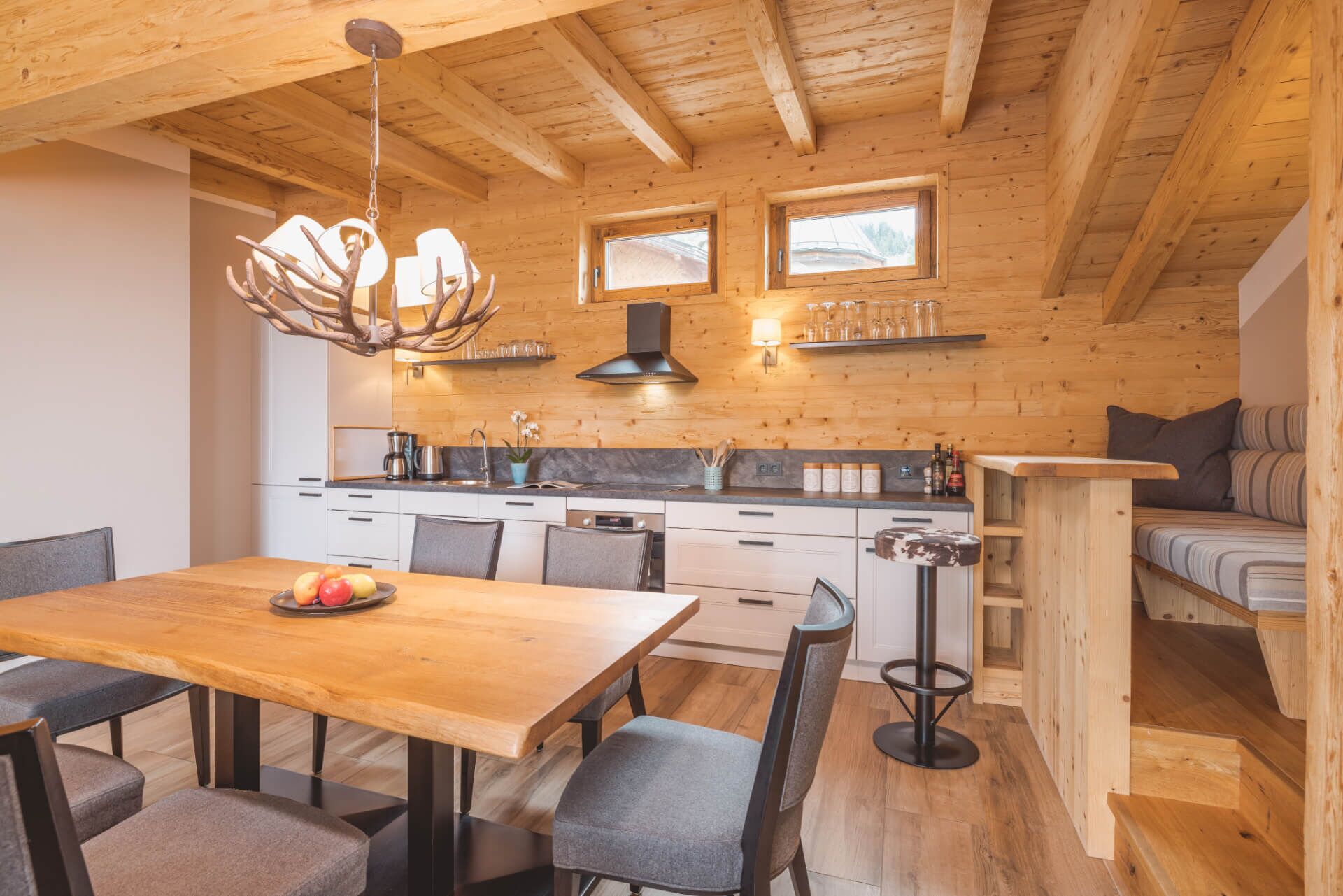 Ein gemütliches Blockhaus-Interieur mit einem Holztisch, Stühlen, einer Küchenzeile mit Herd und einem Sofa.