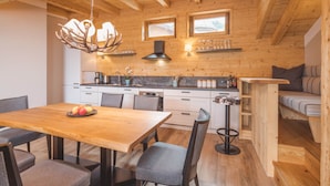 A cozy cabin interior with a wooden dining table, chairs, a kitchen area with a stove, and a sofa.