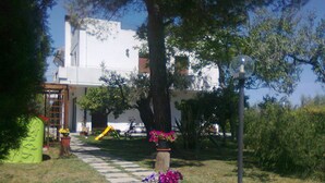 A pathway leading to a white building with a large tree and a playground in the background. - B&B dal Barbarossa (Vasto)